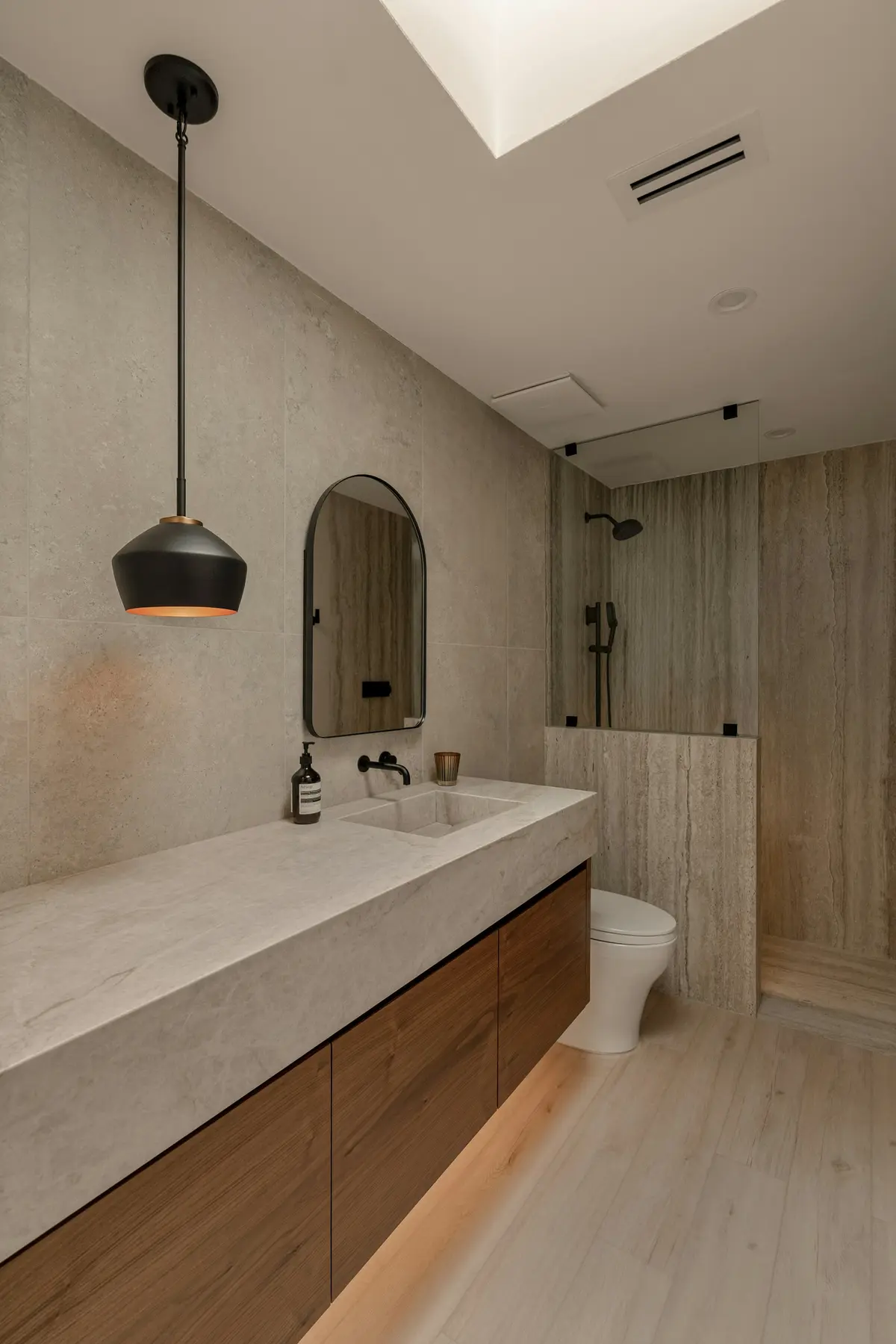 Bathroom vanity set against textured stone-look wall tile under a pendant light